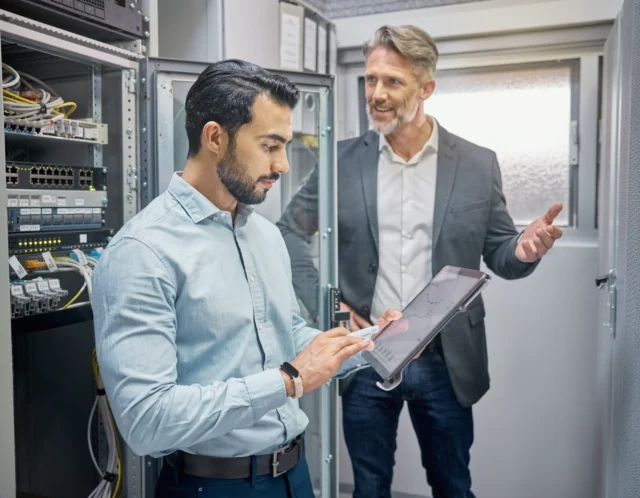 Zwei Personen prüfen gemeinsam Servertechnik und Dokumentation.