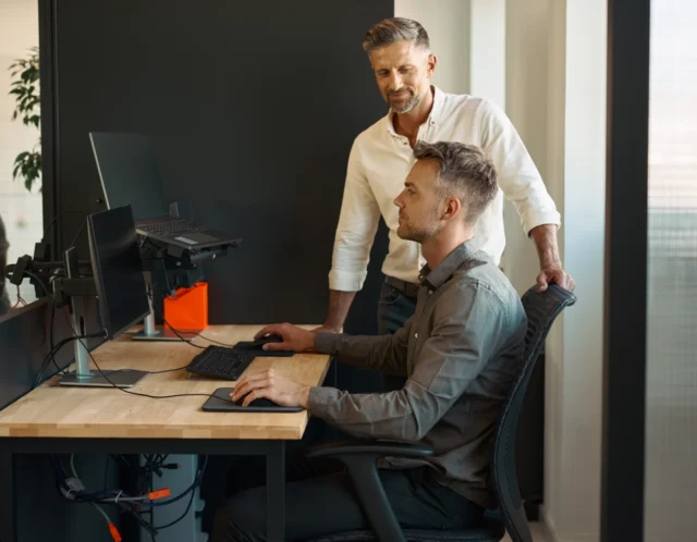 Zwei Personen besprechen die Nutzung eines Computerarbeitsplatzes.